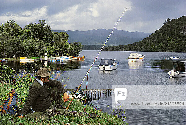 Scotland. Man fishing from the banks of Loch Lomond.