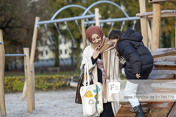A smiling young woman wearing a hijab helps her child on a playground  Netherlands