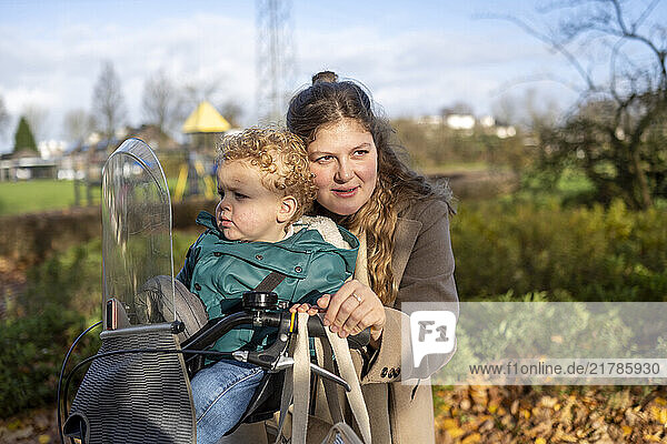 Mother affectionately holds her young child while the child sits in front of the bicycle outdoors on a sunny day  Netherlands