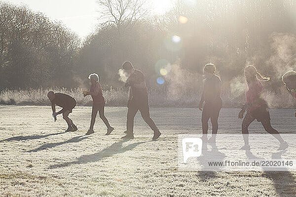 A group of people engaged in outdoor exercise in a frosty field  with sunlight creating lens flares and mist visible from their breath. Sale Water Park  Manchester  UK
