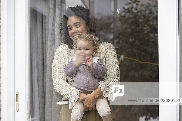 Woman holding a baby  both smiling  looking out from behind a glass window. Netherlands