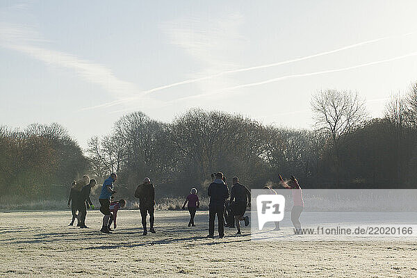 A group of people exercises in a frosty park under a clear sky  surrounded by bare trees and misty grass. Sale Water Park  Manchester  UK