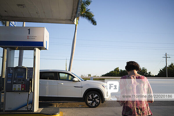Woman in pink top stands at a gas station near a white SUV with palm trees in the background  Florida Keys  USA