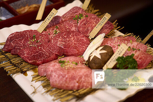 Assorted raw Wagyu beef slices with garnishes on a bamboo mat and white plate. Tokyo  Japan