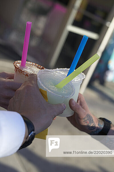 Three hands holding colorful straw drinks in plastic cups outside on a sunny day  Miami  FLorida  USA