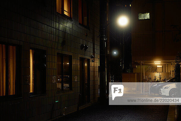 Dimly lit urban alleyway with glowing streetlights and warmly lit windows at night. Tokyo  Japan