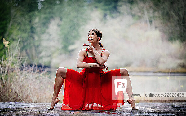 Woman in a red dress performs a yoga pose in a serene outdoor forest setting. USA