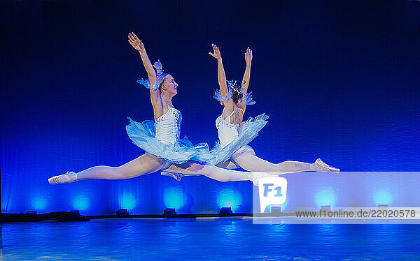 Two ballerinas in blue tutus perform ballet leaps on stage with dramatic blue lighting. The Nutcracker  Bainbridge Island  USA