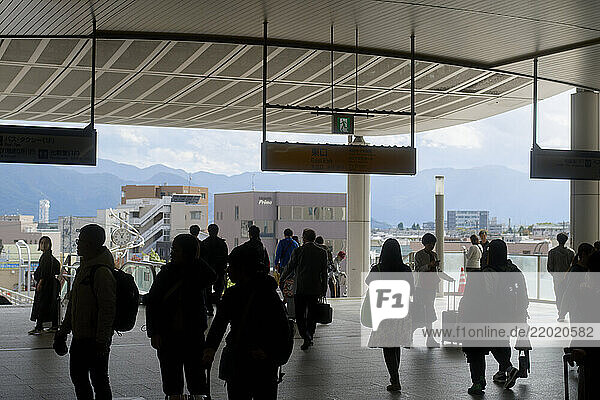 Busy train station platform with people silhouetted against a bright cityscape background. Nagano  Japan
