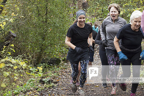 A group of women of varying ages are energetically running through a forest trail in autumn  surrounded by green and yellow foliage. Sale Water Park  Manchester  UK