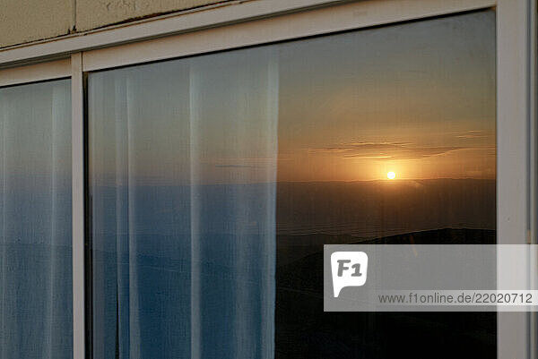 Sunset reflected on a hotel room window with curtains softly illuminated by the evening light. Israel