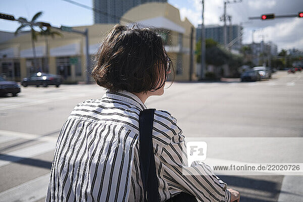 Woman with short hair crosses an urban street on a sunny day  wearing a striped shirt  Miami  Florida  USA