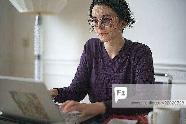 Woman in deep focus working on a laptop at a table with a mug and books.