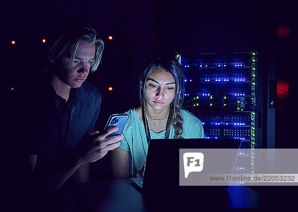 Female and male technicians using laptop in server room