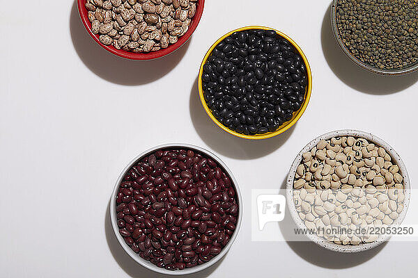 Overhead view of bowls of various beans on white background