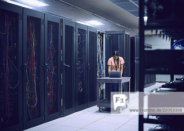 Female technician using laptop in server room