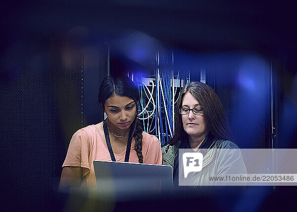 Two female technicians using laptop in server room
