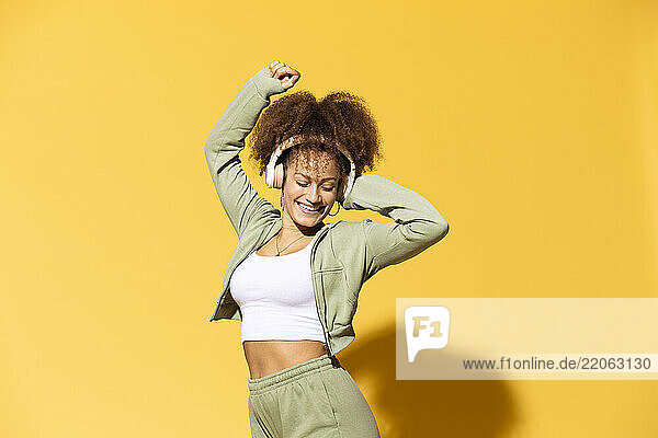 Smiling woman with wireless headphones standing in front of yellow background