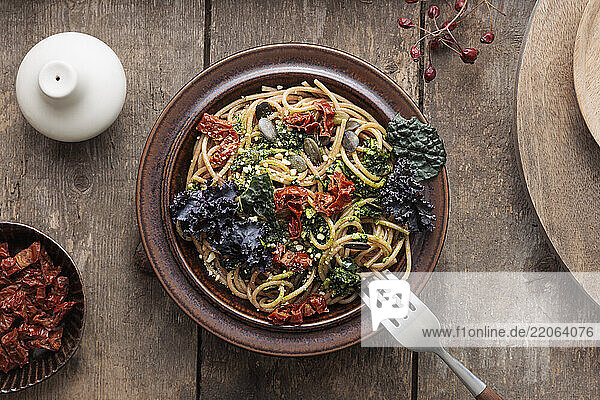 Spaghetti with kale  pesto  and dried tomatoes on a rustic wooden table