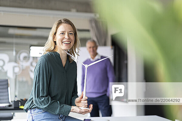 Happy businesswoman holding wind turbine model sitting in office