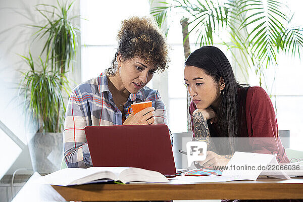 Two women sharing laptop at table in office