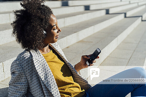 Beautiful woman sitting on stairs in the city  using smartphone  listening music with headphones