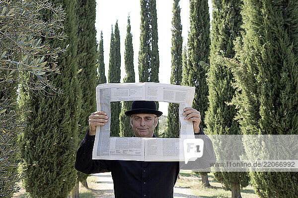 Italy  Tuscany  man surrounded by cypresses reading newspaper with a hole