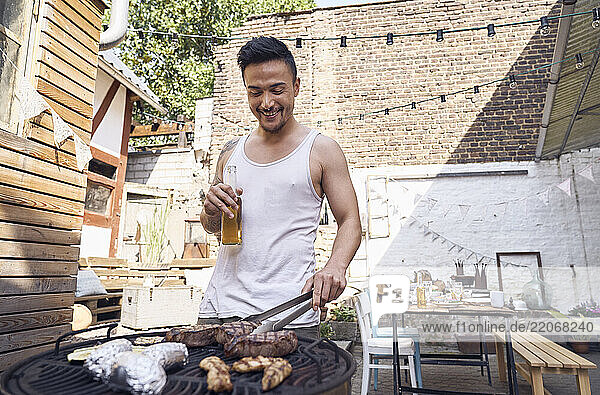 Young man preparing meat on a barbecue grill in a backyard