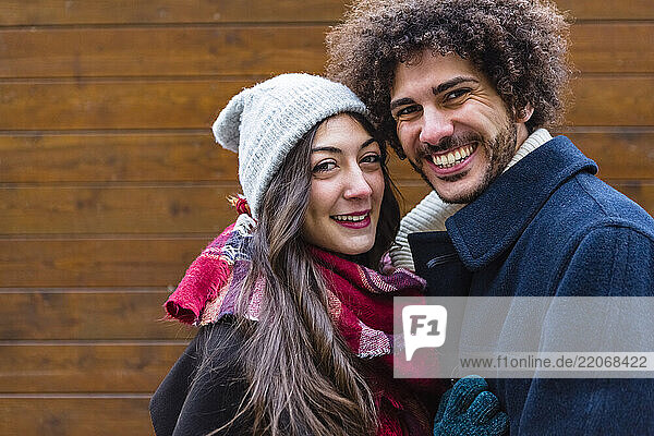 Portrait of happy young couple in winterwear in front of wooden wall
