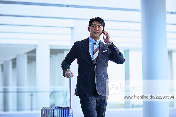 Japanese Businessman In Suit And Tie Holding Suitcase And Talking On Cell Phone