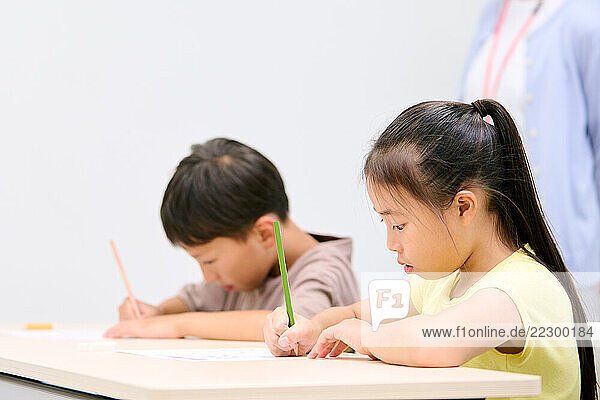 Two Children Sitting At A Desk With Pencils
