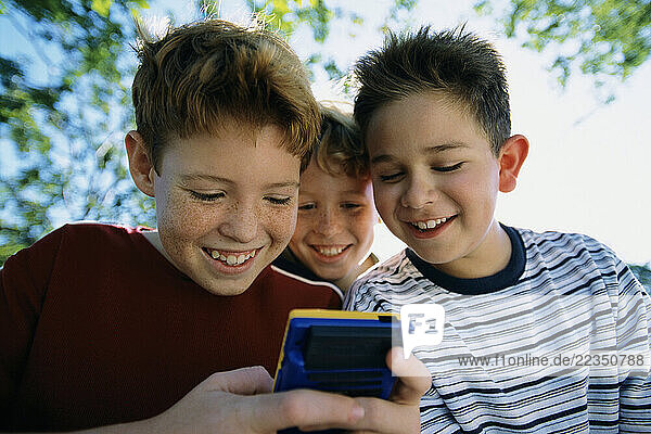Three Boys Playing Handheld Video Game Outdoors