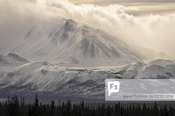 Mount Decoeli is shrouded in the mists of the Yukon during spring. This creates a dramatic atmosphere. The rising sun illuminates the clouds; Haines Junction  Yukon  Canada