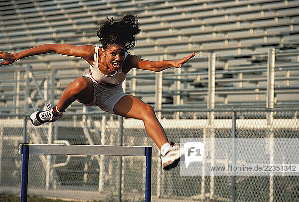 Woman Jumping over Hurdles in Stadium