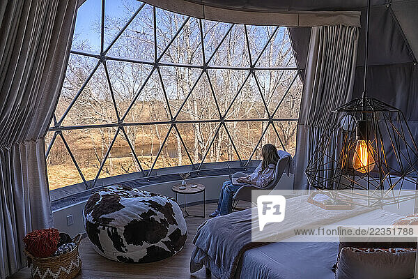 Woman sitting in a chair working on a computer while enjoying the view from a geodosic dome; Elderbank  Nova Scotia  Canada