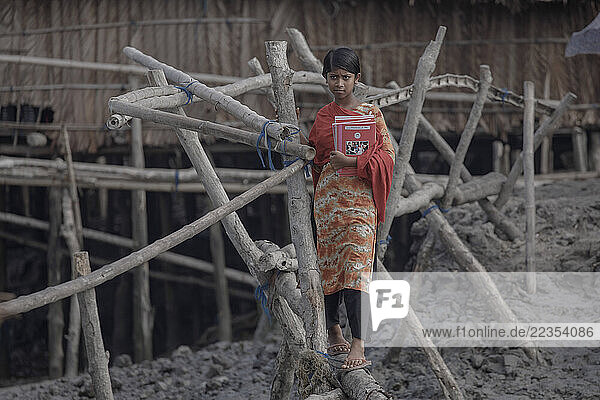 Girl going to school crossing through a bamboo bridge at the village Kalabogi which is next to the Sunderban forest in Bangladesh on 26 April 2021. Every year the water level of the river increases more and more. The villagers make the bamboo bridge so at least they can use it for emergency time; Khulna  Dhaka  Bangaldesh