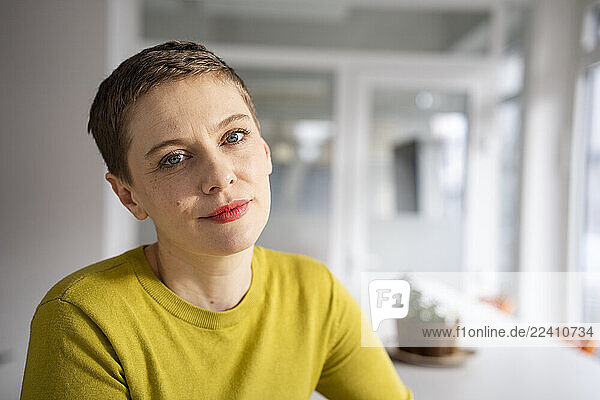 Woman in a green sweater posing confidently in a modern office environment