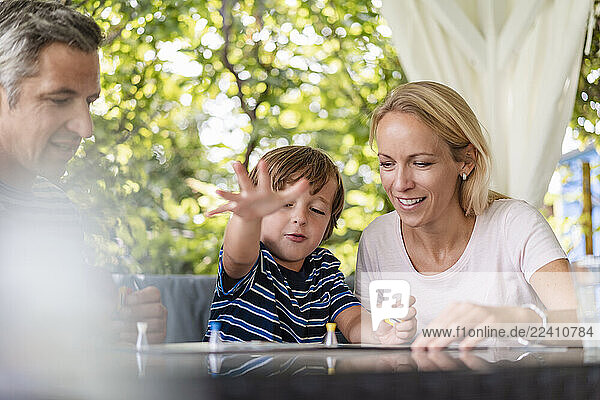 Happy parents and son playing a board game on terrace