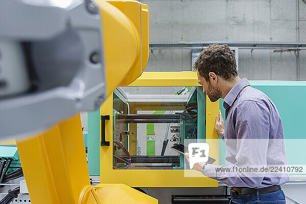 Man in a production hall with an industrial robot and tablet