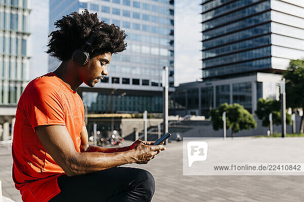 Young sportsman sitting on a bench  using smartphone and listening to music