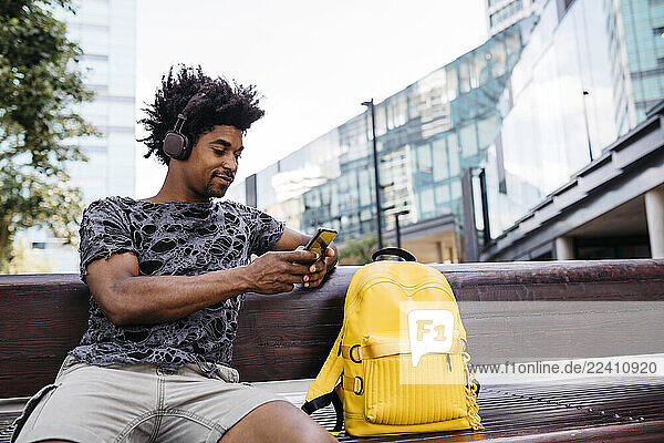 Man sitting on the bench listening music with headphones while using mobile phone  Barcelona  Spain