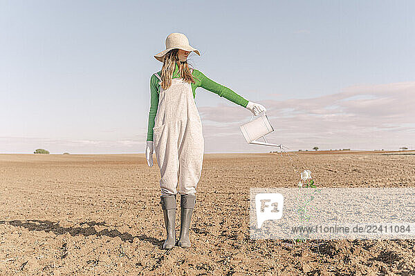 Woamn standing on barren field  watering flower
