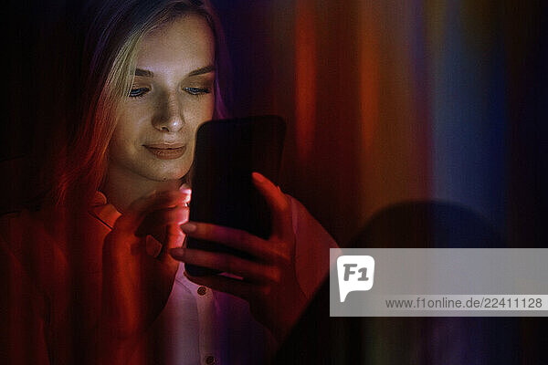 Woman using smartphone at night with neon light reflection