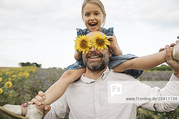 Sunflowers covering eyes of playful man with daughter in a field