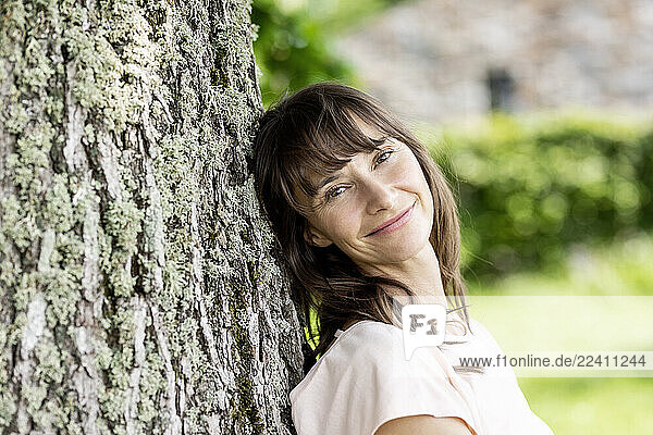 Portrait of smiling brunette woman leaning against a tree trunk
