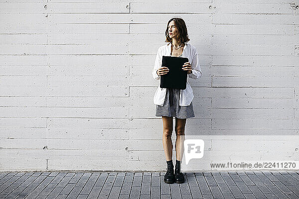 Pretty woman standing in front of building  carrying folder