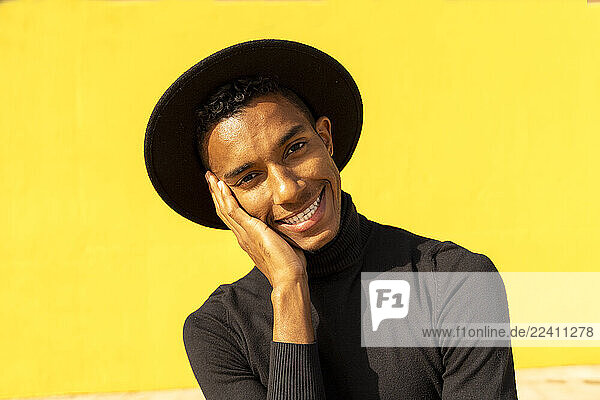 Portrait of young man  wearing black in front of yellow wall  hand on face
