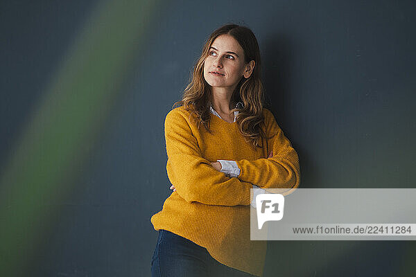 Portrait of a thoughtful woman in a yellow sweater standing indoors with arms crossed