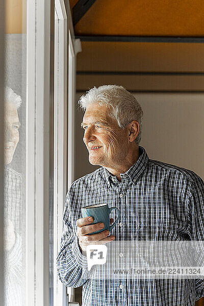 Smiling senior man looking at home through window