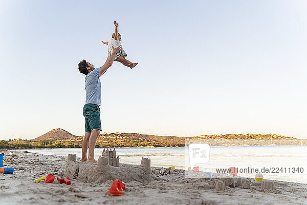 Sand castle and happy father lifting up daughter on the beach